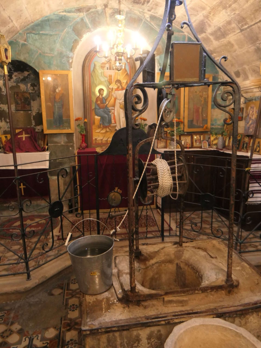 The stone mouth of a deep well with a winding drum, a rope and a metal bucket standing over it