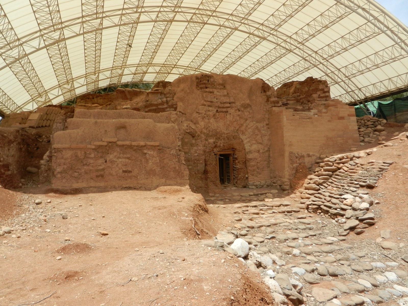 The excavated mudbrick gateway at Tel Dan, its arched opening intact, with a stone approach ramp and a modern canopy overhead